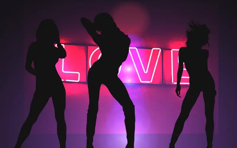 Silhouettes of Women Dancing in front of a glowing pink neon LOVE sign