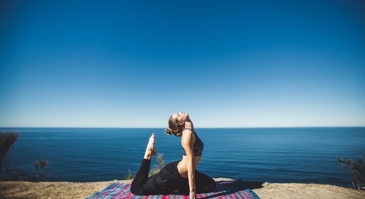 Get more flexible - a woman does Yoga on the beach with the blue ocean behind her